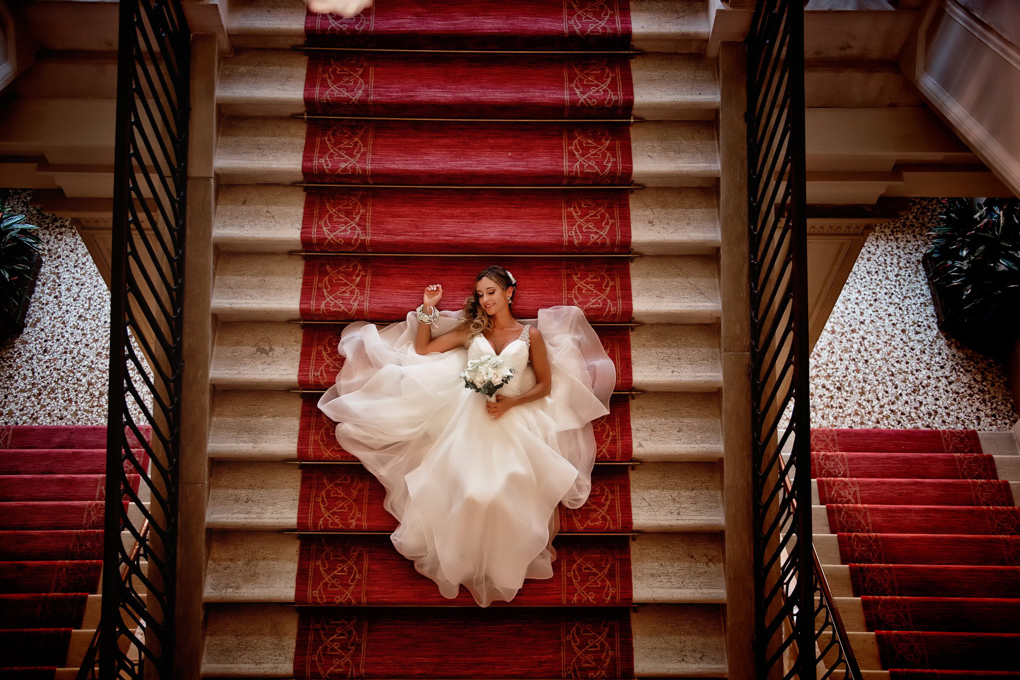 A bride in a flowing white gown relaxes on a grand staircase bathed in warm, natural light, capturing an elegant Venice.