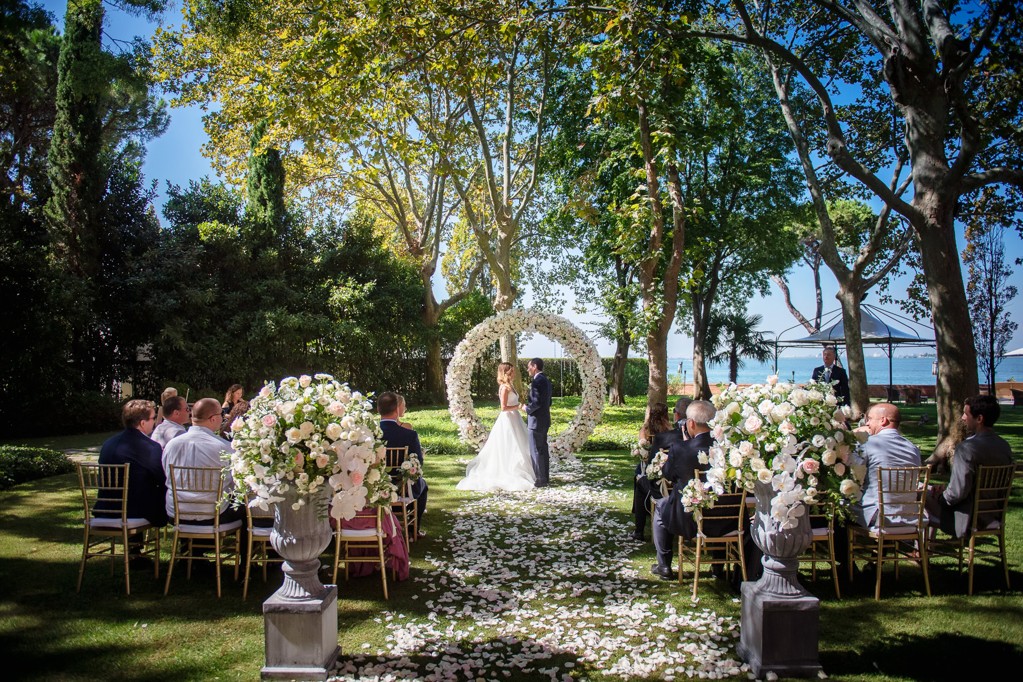 A lush outdoor wedding ceremony set among tall trees and vibrant greenery in Venice.