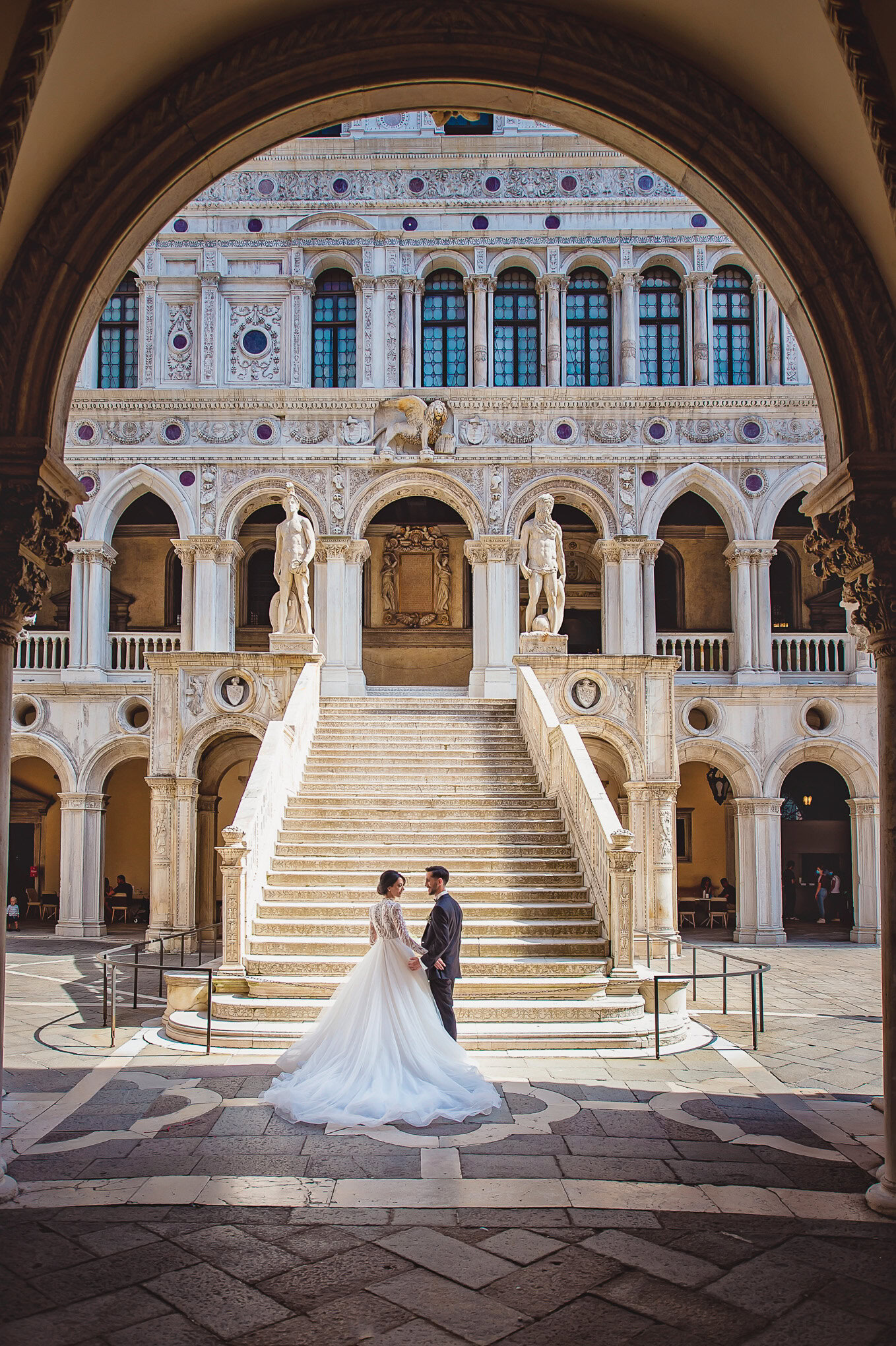 Elegant bride and groom share a romantic moment beneath Venice’s historic arches, bathed in soft natural light inside a.