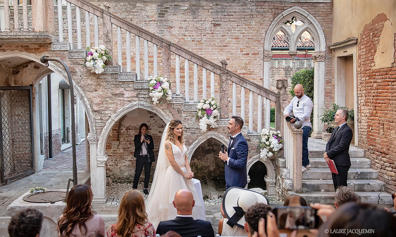 Elegant bride and groom exchanging vows in a historic Venetian courtyard with soft natural light and floral decorations.