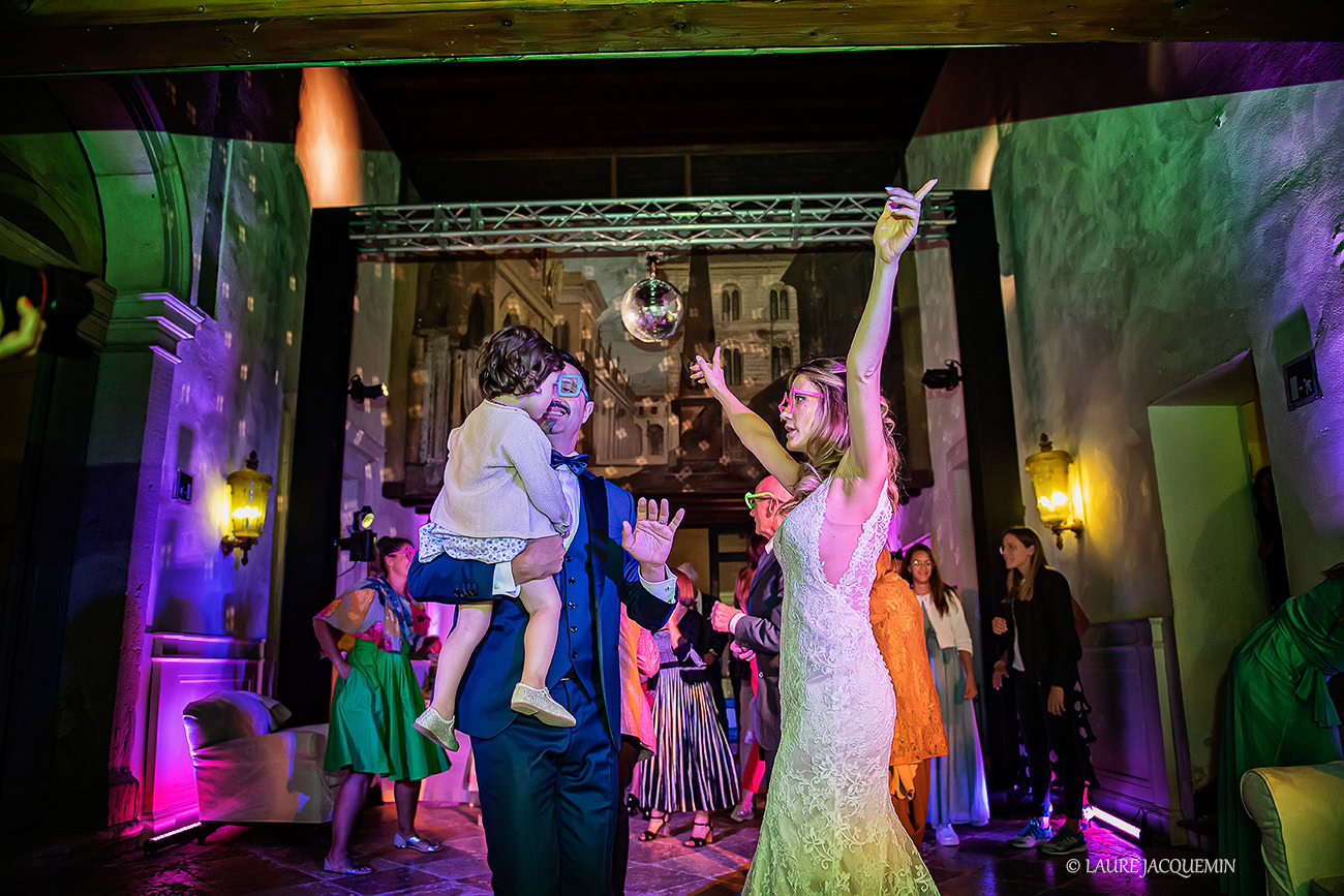 Elegant wedding scene in Venice with dancing guests under colorful lights and historic architecture in the background.