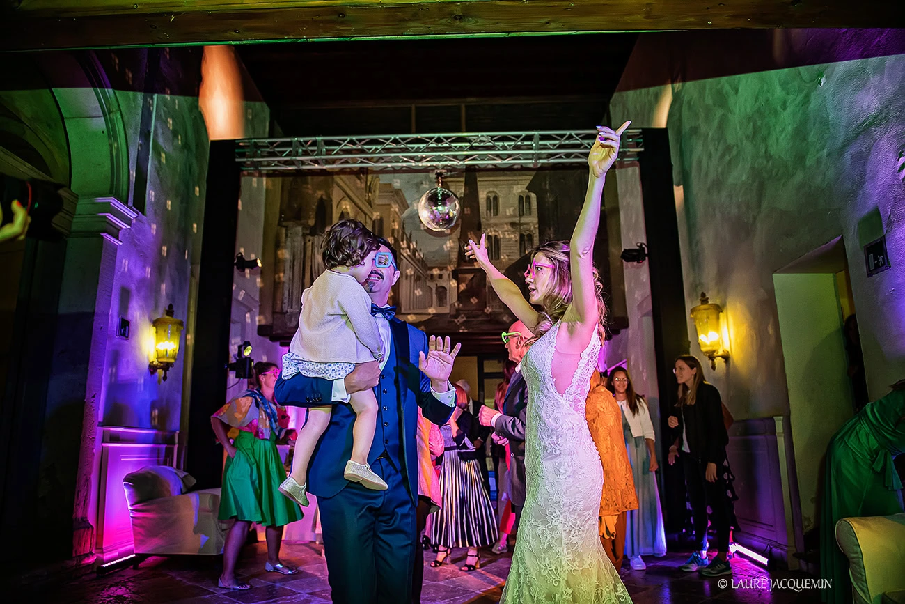 Elegant wedding scene in Venice with dancing guests under colorful lights and historic architecture in the background.