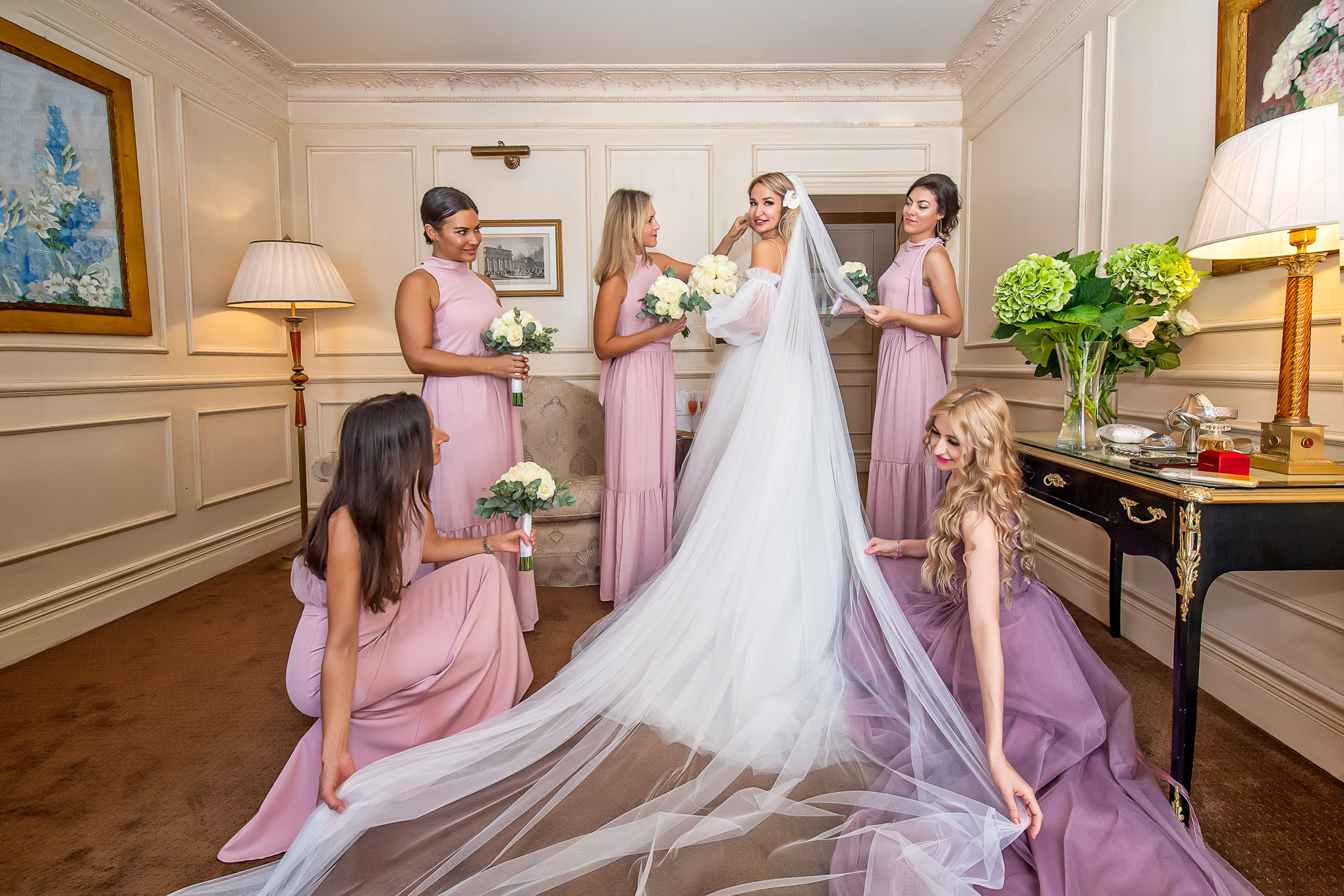 An elegant bride in a flowing white gown shares a tender moment with her bridesmaids in a beautifully decorated Venetian.