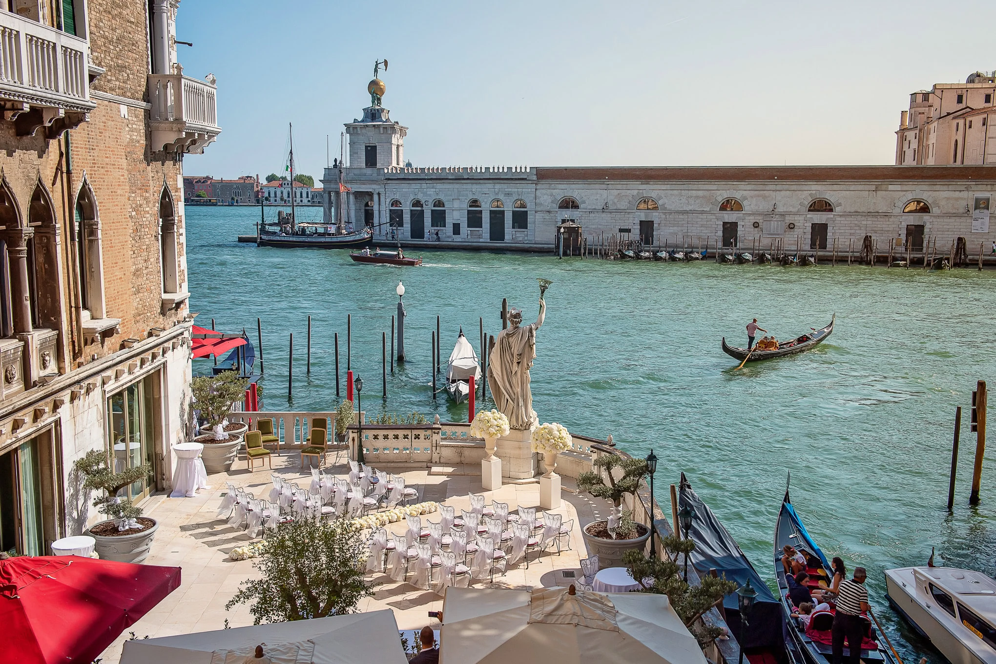 A lush outdoor wedding setup overlooking Venice's Grand Canal with historic architecture and gondolas under bright dayli.