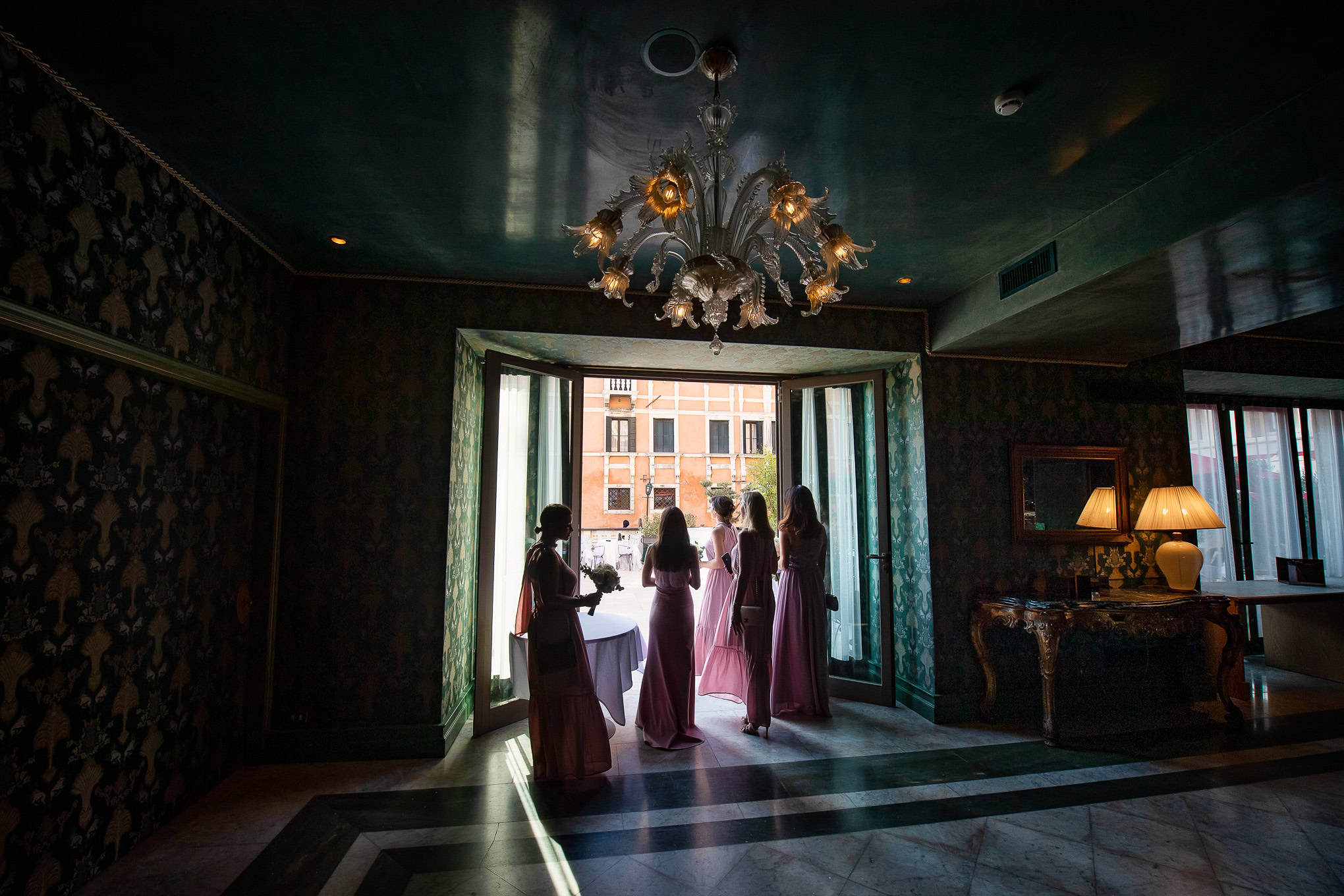 Elegant wedding moment in Venice with bridesmaids in pink dresses by a large window, soft natural light illuminating the.