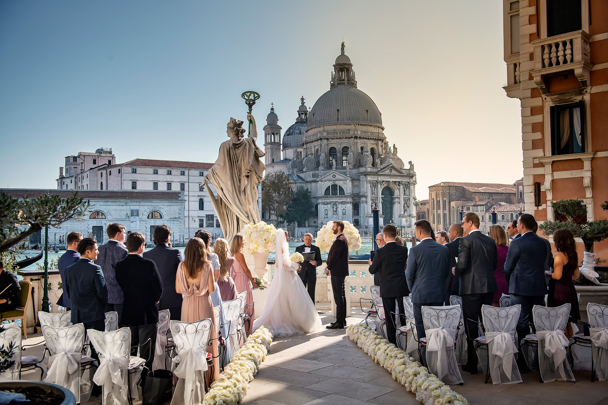 Elegant wedding ceremony on a terrace in Venice with historic architecture and soft sunset light illuminating the scene.