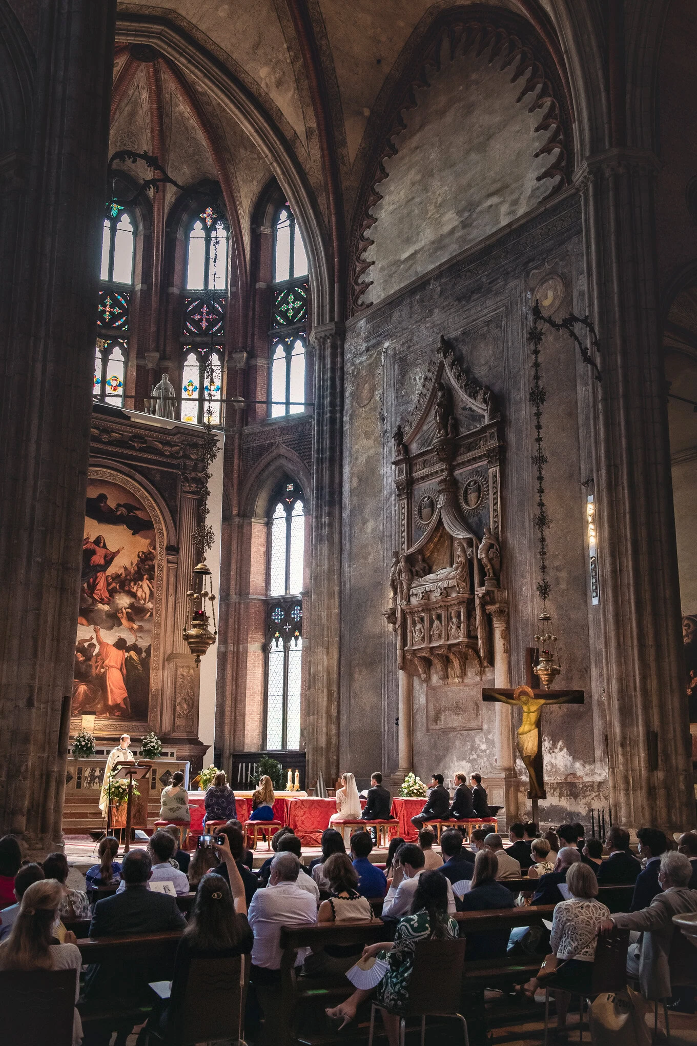 A couple exchanging vows inside a historic Venetian church illuminated by soft natural light streaming through stained g.