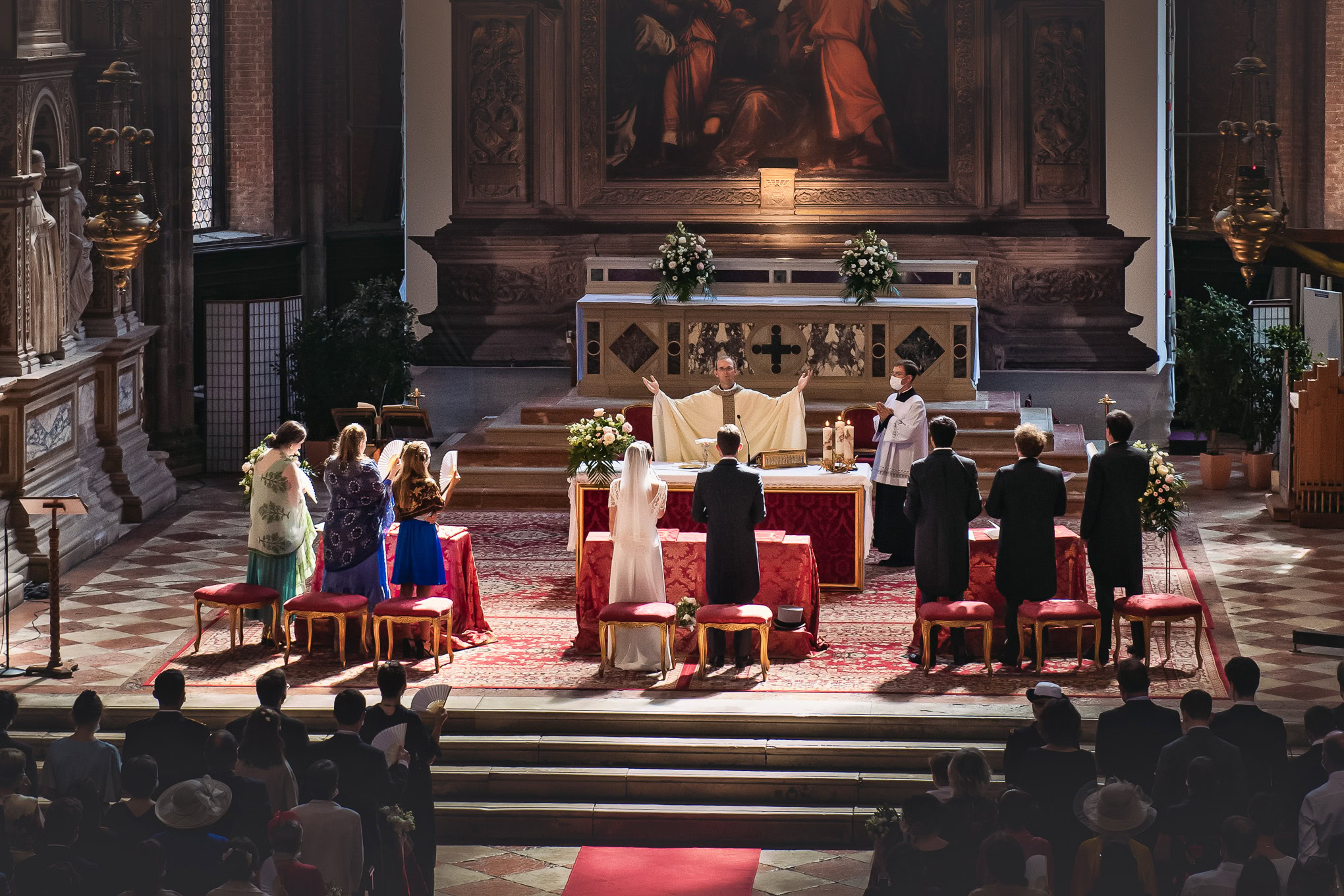 A couple exchanging vows during a wedding ceremony inside a historic Venetian church with ornate woodwork and soft natur.