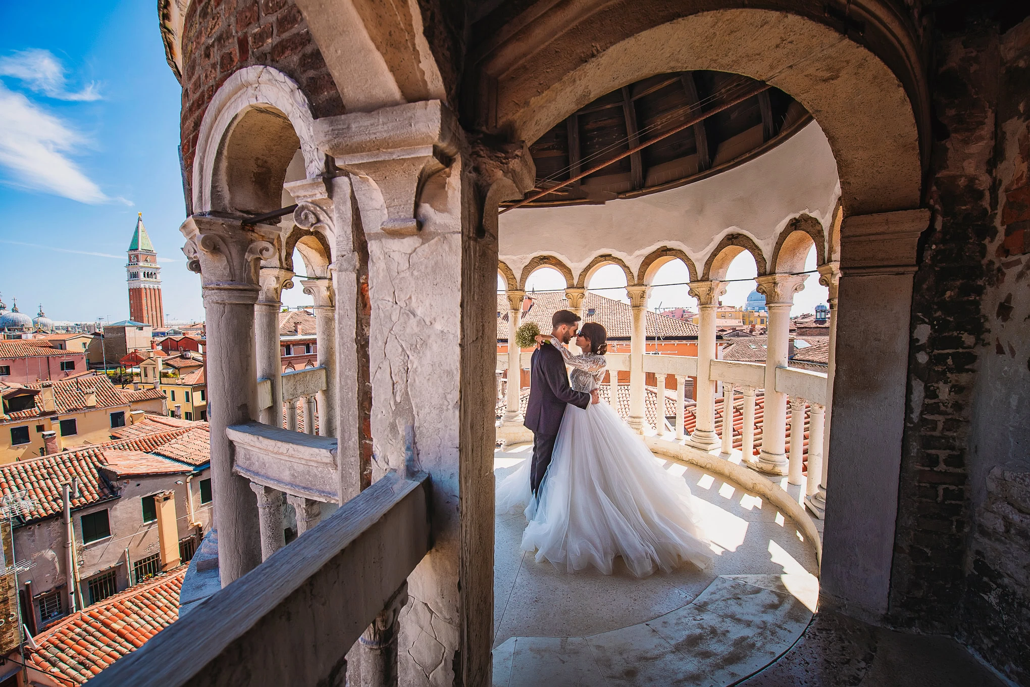 A couple shares a romantic moment on a Venetian balcony with historic architecture and a scenic cityscape in the backgro.