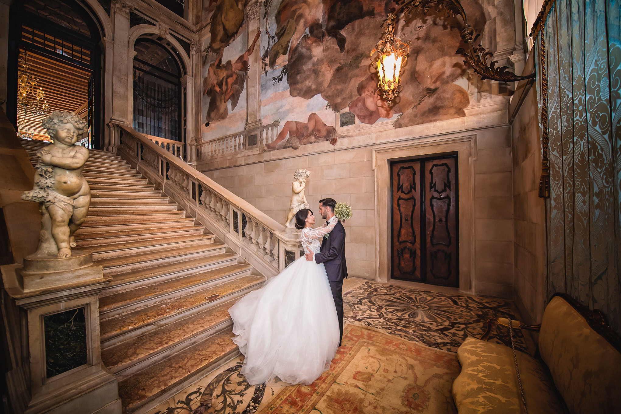 A couple shares a romantic moment on a grand Venetian staircase inside an ornate historic building, illuminated by warm,.