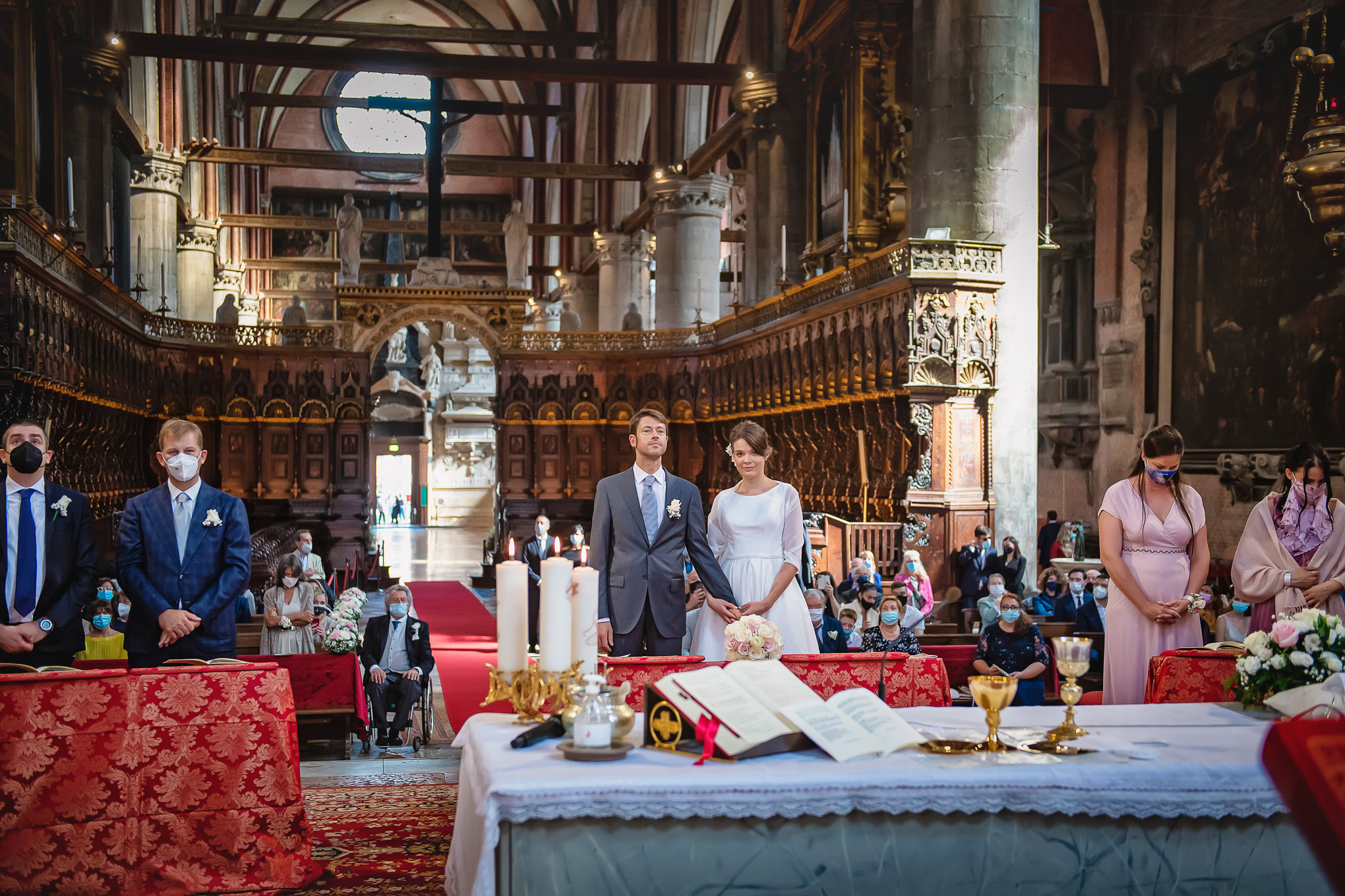 A couple stands solemnly at the altar during their wedding ceremony inside a grand Venetian church with ornate woodwork.