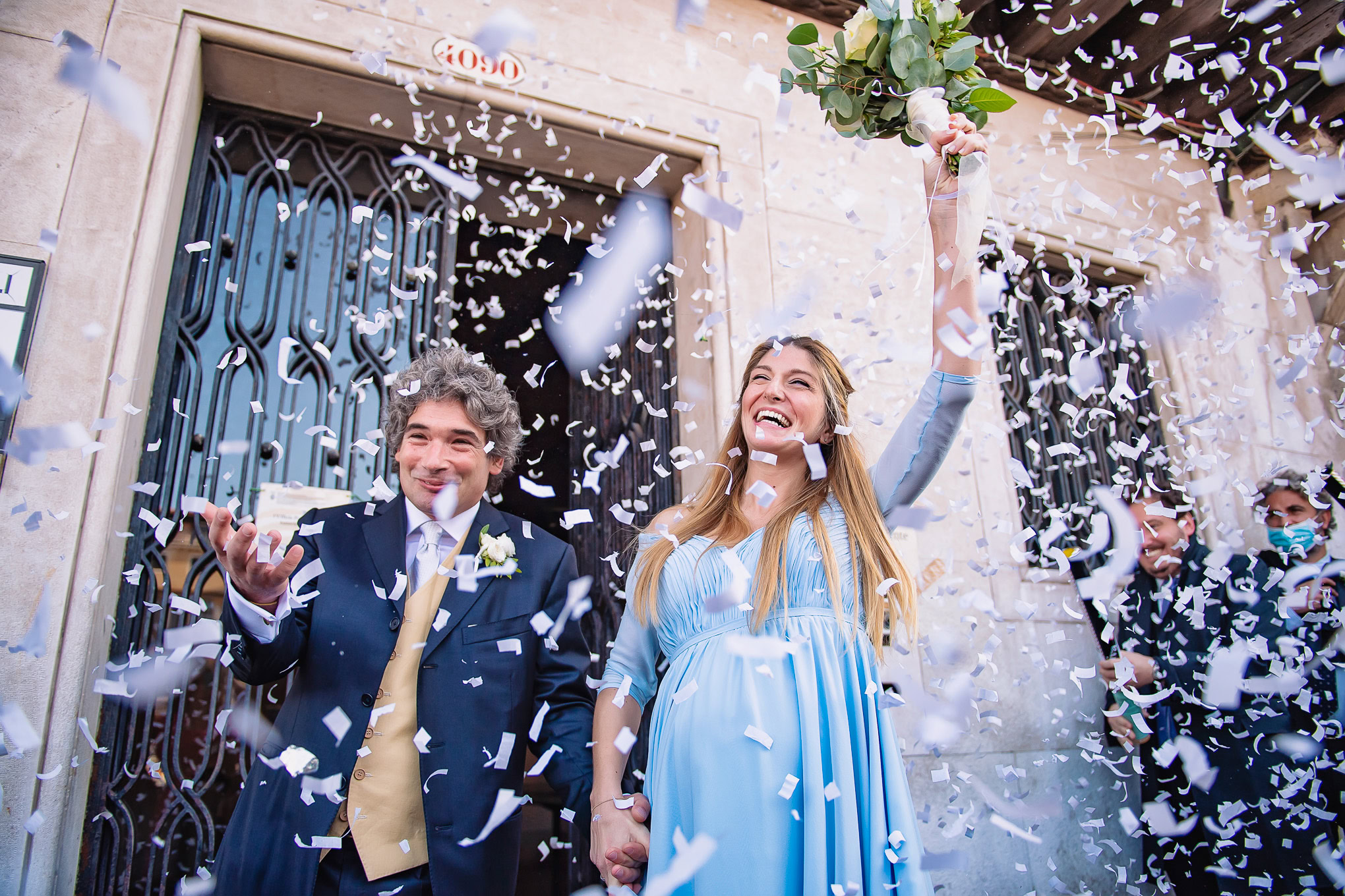 Joyful newlyweds celebrating with confetti outside a historic Venetian building under soft daylight.