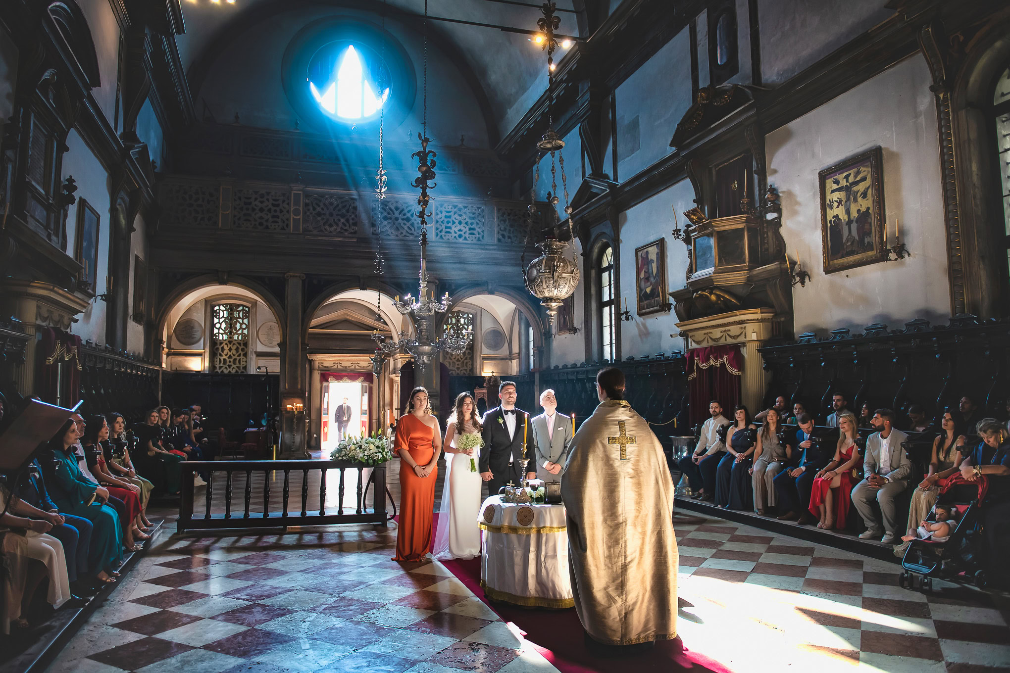 A couple getting married in a historic Venetian church with guests seated on both sides.