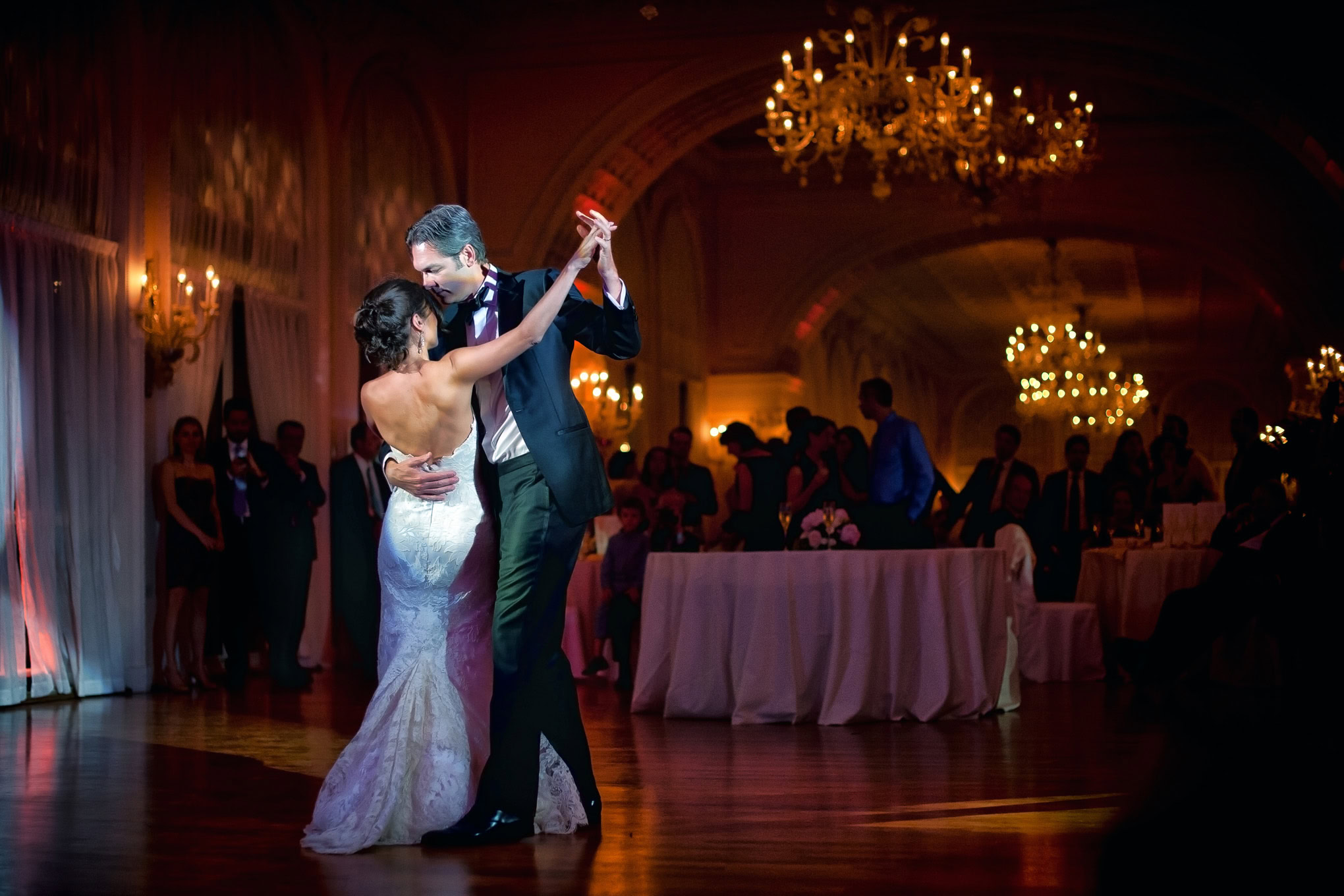 Elegant couple dancing closely during their wedding reception in a grand Venetian ballroom illuminated by warm chandelie.