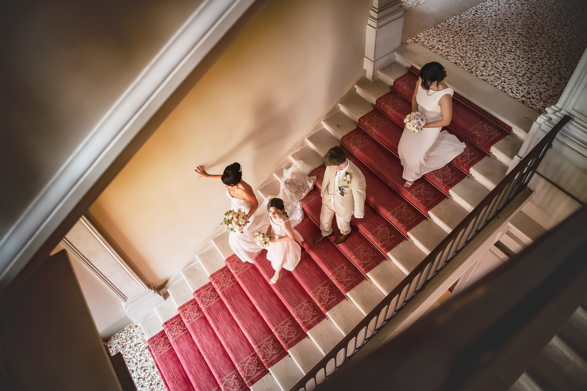 Elegant scene of bridesmaids and bride on a Venetian staircase with warm lighting and classic decor.