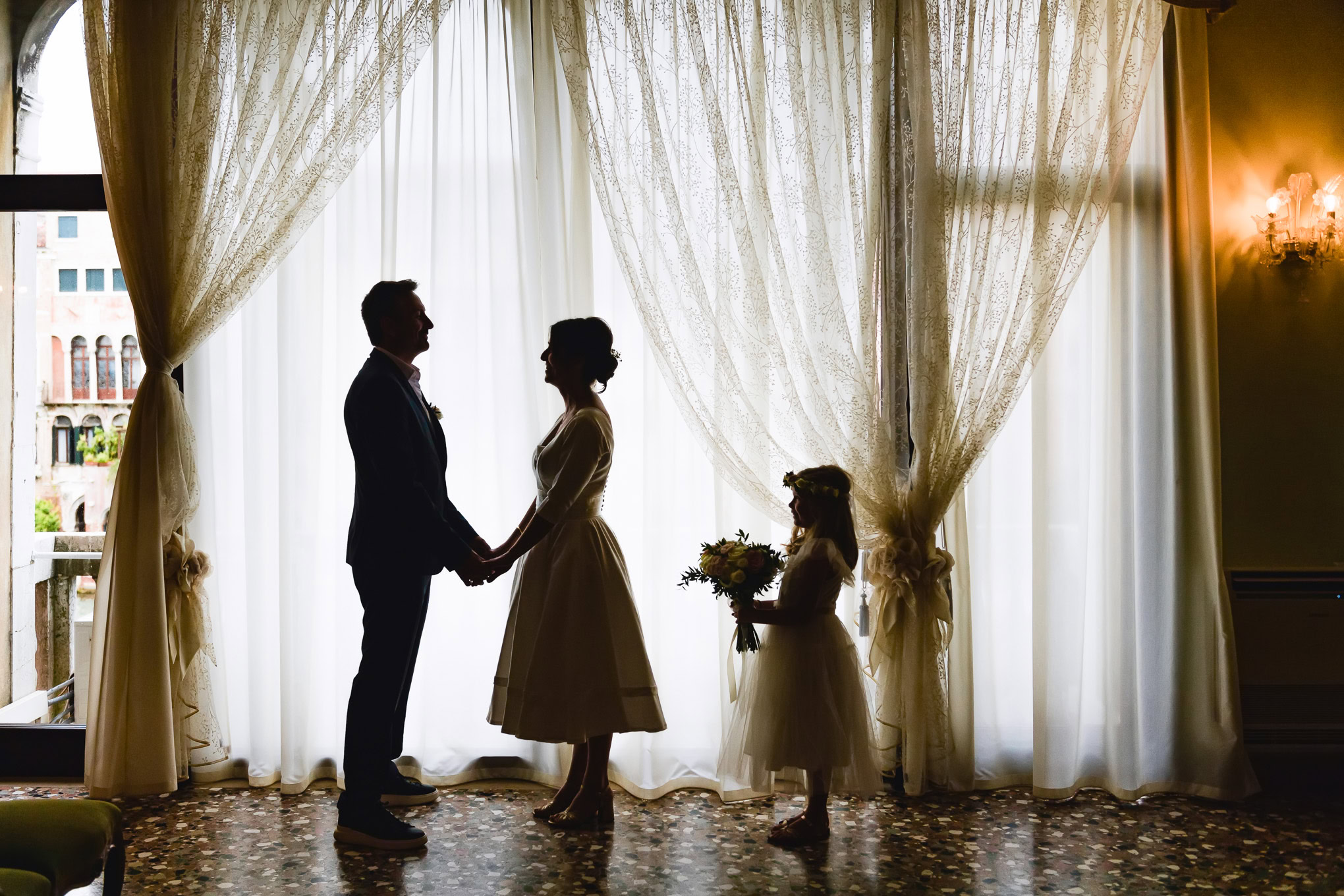 Elegant wedding moment captured indoors with natural light streaming through sheer curtains in a historic Venetian setti.