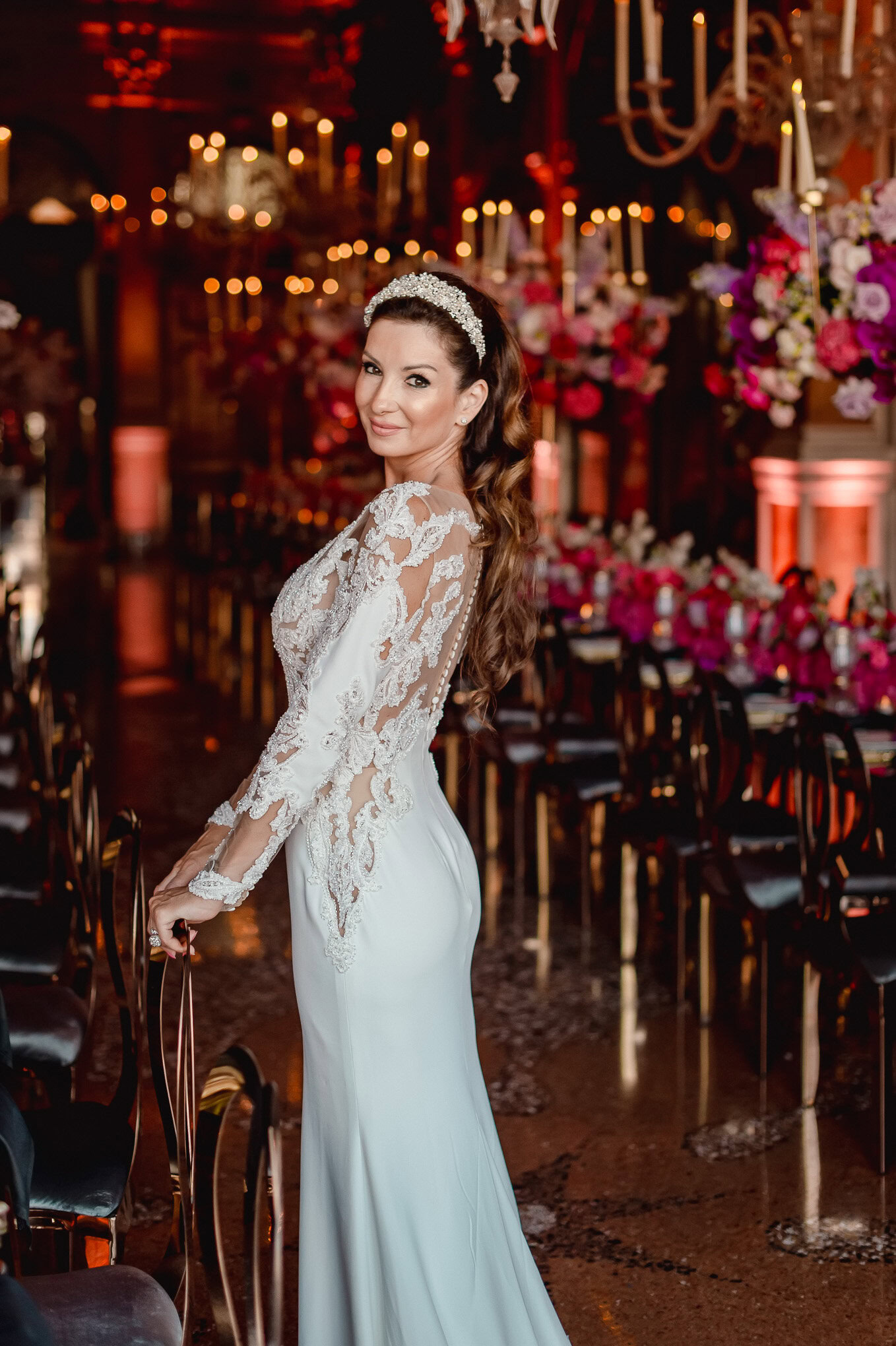Elegant bride in a lace gown and tiara, standing in a romantic Venetian wedding reception with warm candlelight and flor.