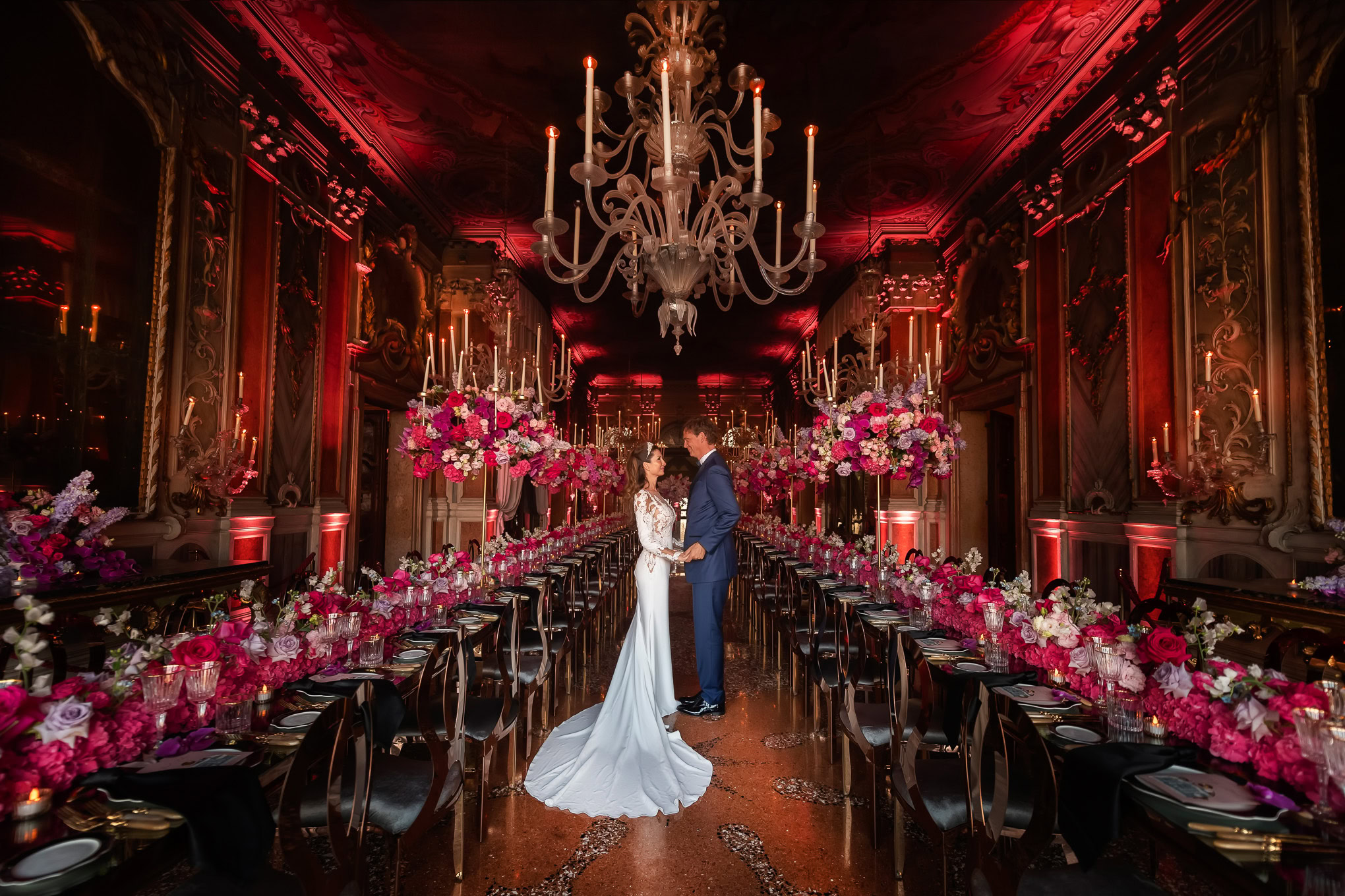 A couple in wedding attire standing in an opulent Venetian-style ballroom with elaborate gold decor and romantic lightin.