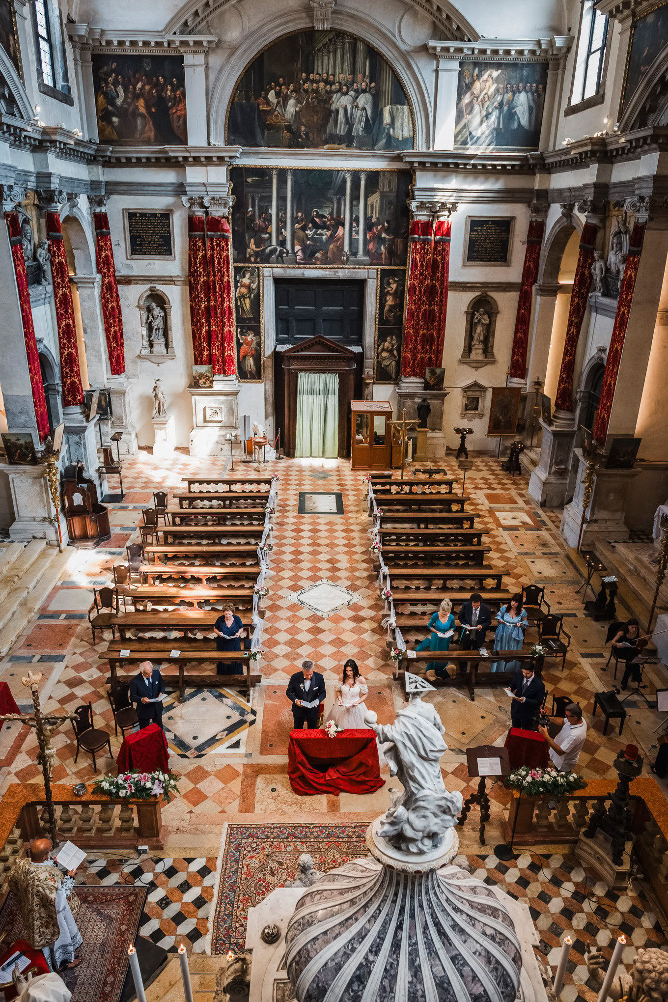 Elegant wedding ceremony inside a grand Venetian church with ornate architecture, warm lighting, and a romantic atmosphe.