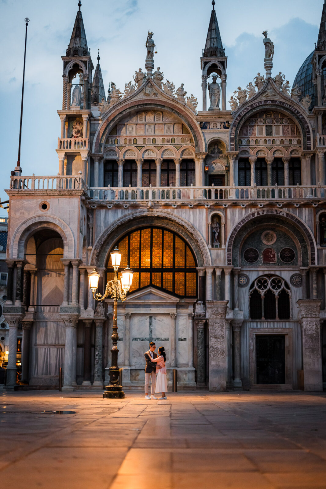 Couple before illuminated Basilica San Marco facade at dusk