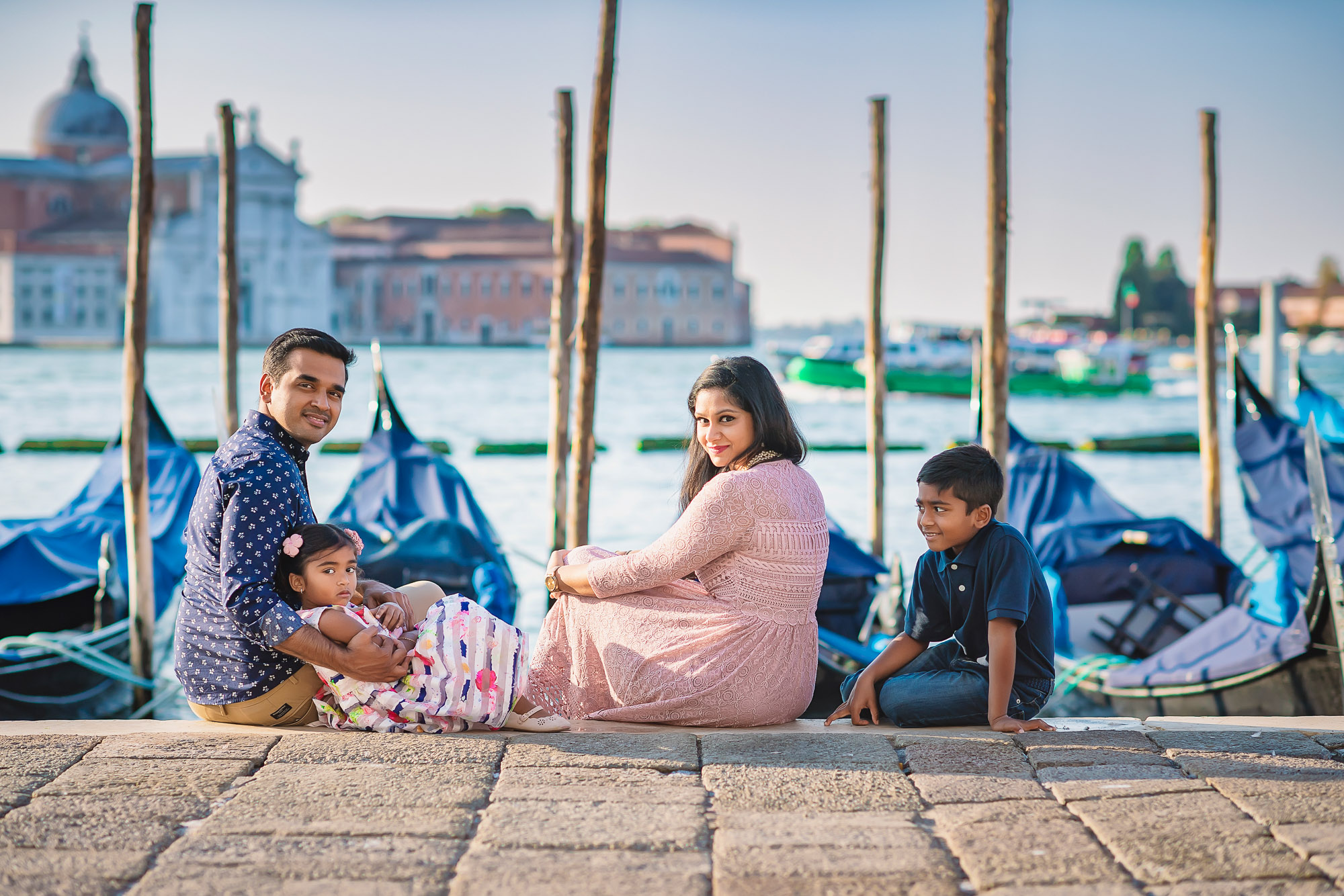 Venice waterfront with family sitting on stone dock, parents and children smiling, child looking at camera, during late.