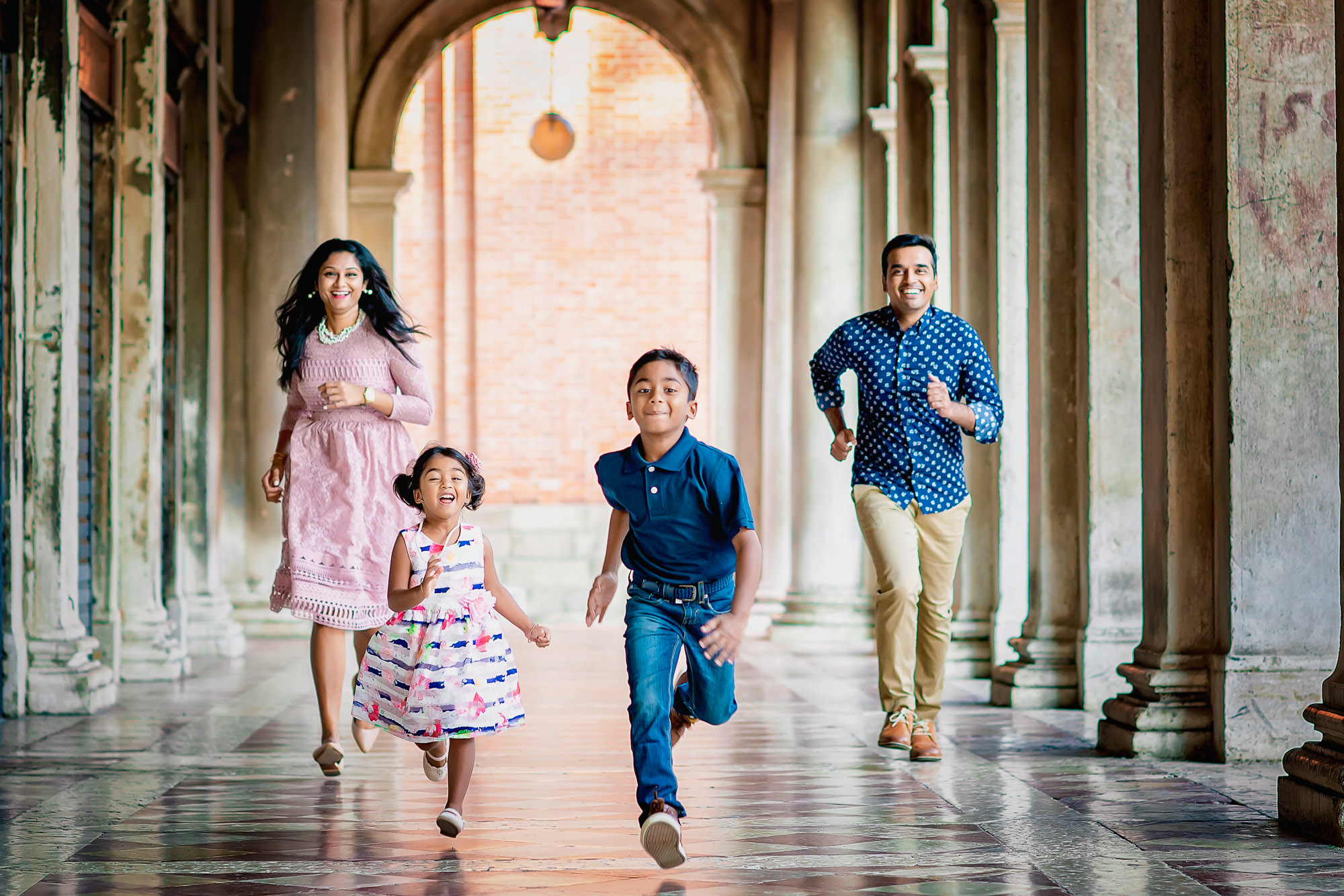 Family walking through Venice arcade with children smiling and looking at camera during daytime.