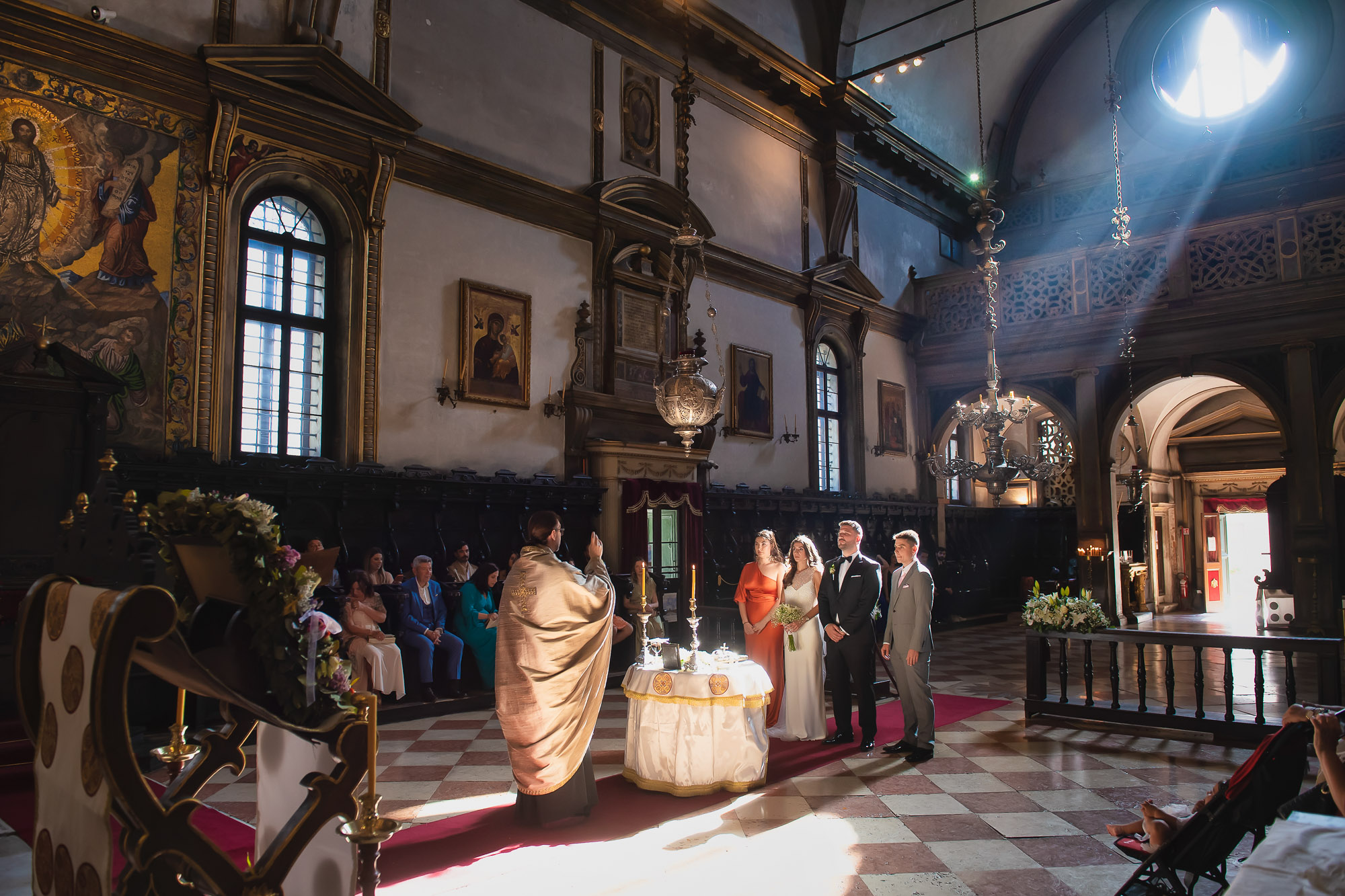 Venice church during a Catholic wedding ceremony with the priest blessing the couple. Sunlight streams through the windo.