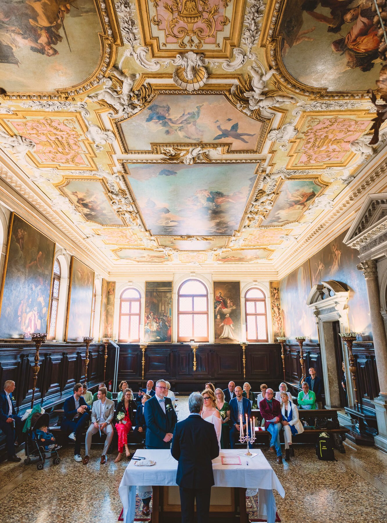 Elegant wedding ceremony inside the historic Scuola Grande dei Carmini in Venice, featuring stunning Tiepolo ceiling fre.