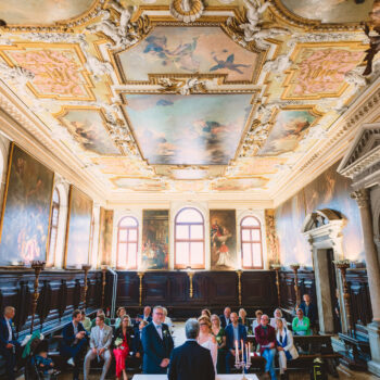 Elegant wedding ceremony inside the historic Scuola Grande dei Carmini in Venice, featuring stunning Tiepolo ceiling fre.