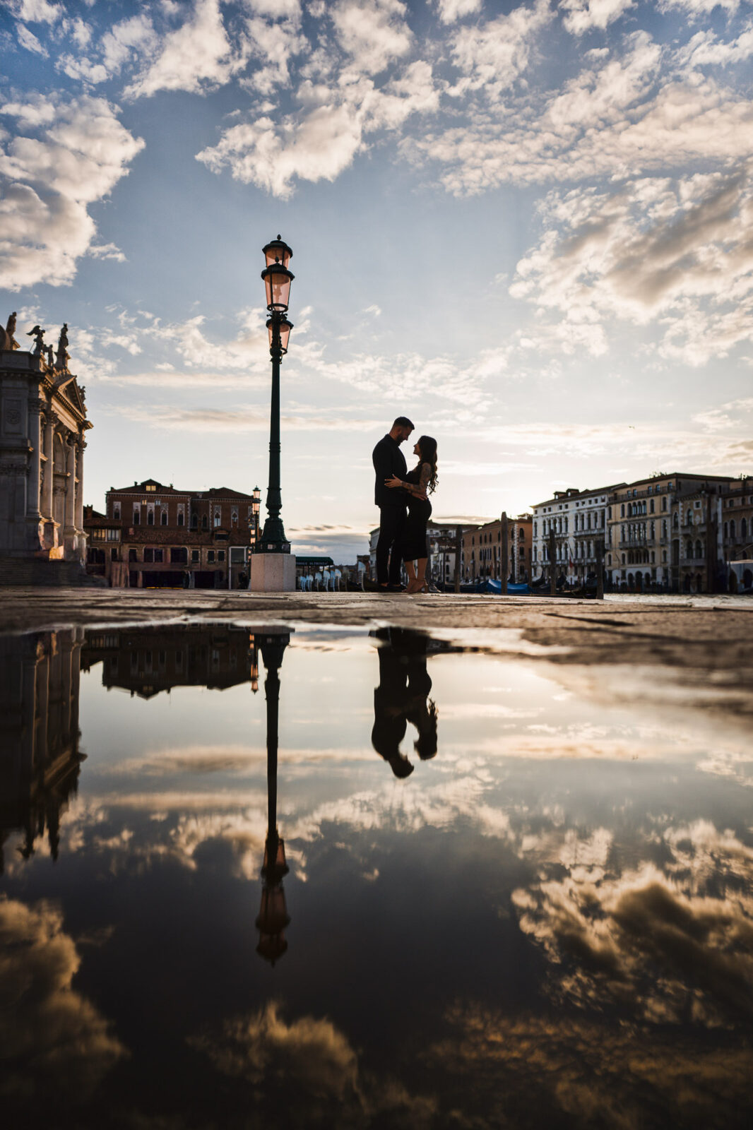 Romantic couple proposing in Venice square during sunset with historic buildings and cloudy sky.