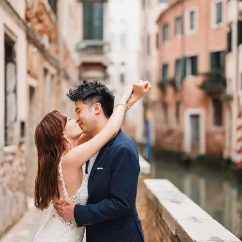 Engagement-Photos-in-Venice (7) Elegant couple kissing in Venice, romantic wedding proposal on historic canal bridge.