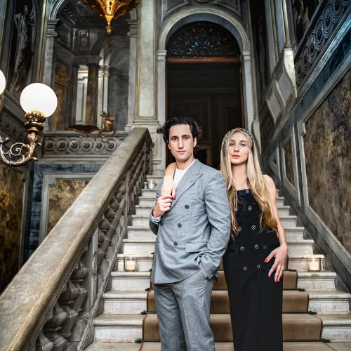 engagement photos tips in Venice (35) Elegant couple in fashionable attire at historic Venetian staircase, showcasing luxurious ambiance and opulent decor.