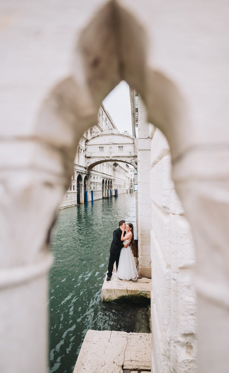 honeymoon couple framed by gothic Venetian arch near canal