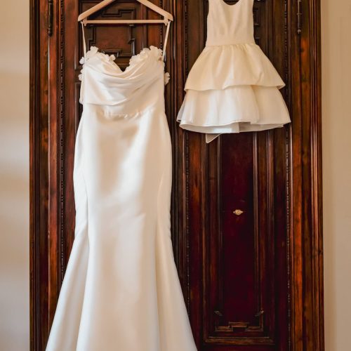 venice-photography-wedding-church-san-giorgio-greci (4) Elegant wedding dress and flower girl dress hanging on a wooden wardrobe in a stylish bridal preparation room.